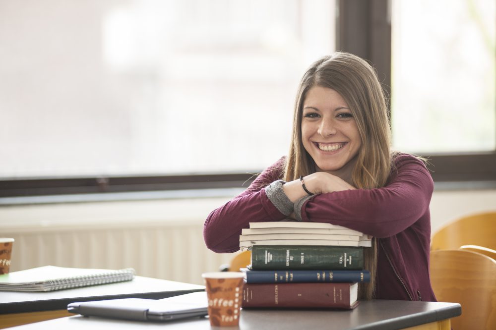 Étudiante souriante accoudée à des livres